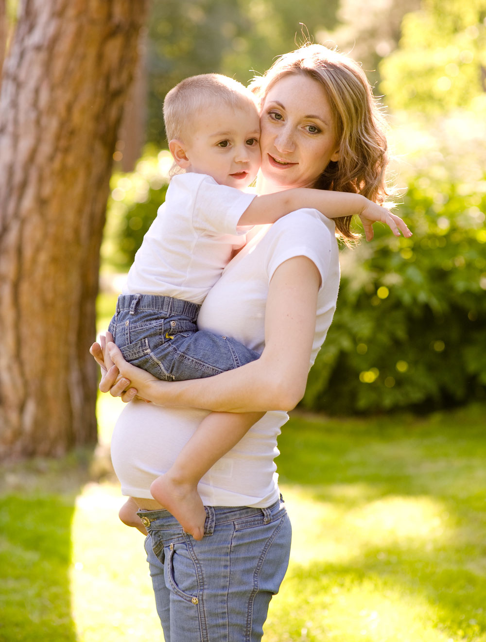 Soins de grossesse – Étreinte aimante Une femme enceinte tient un enfant dans ses bras, à l'extérieur dans un environnement verdoyant.