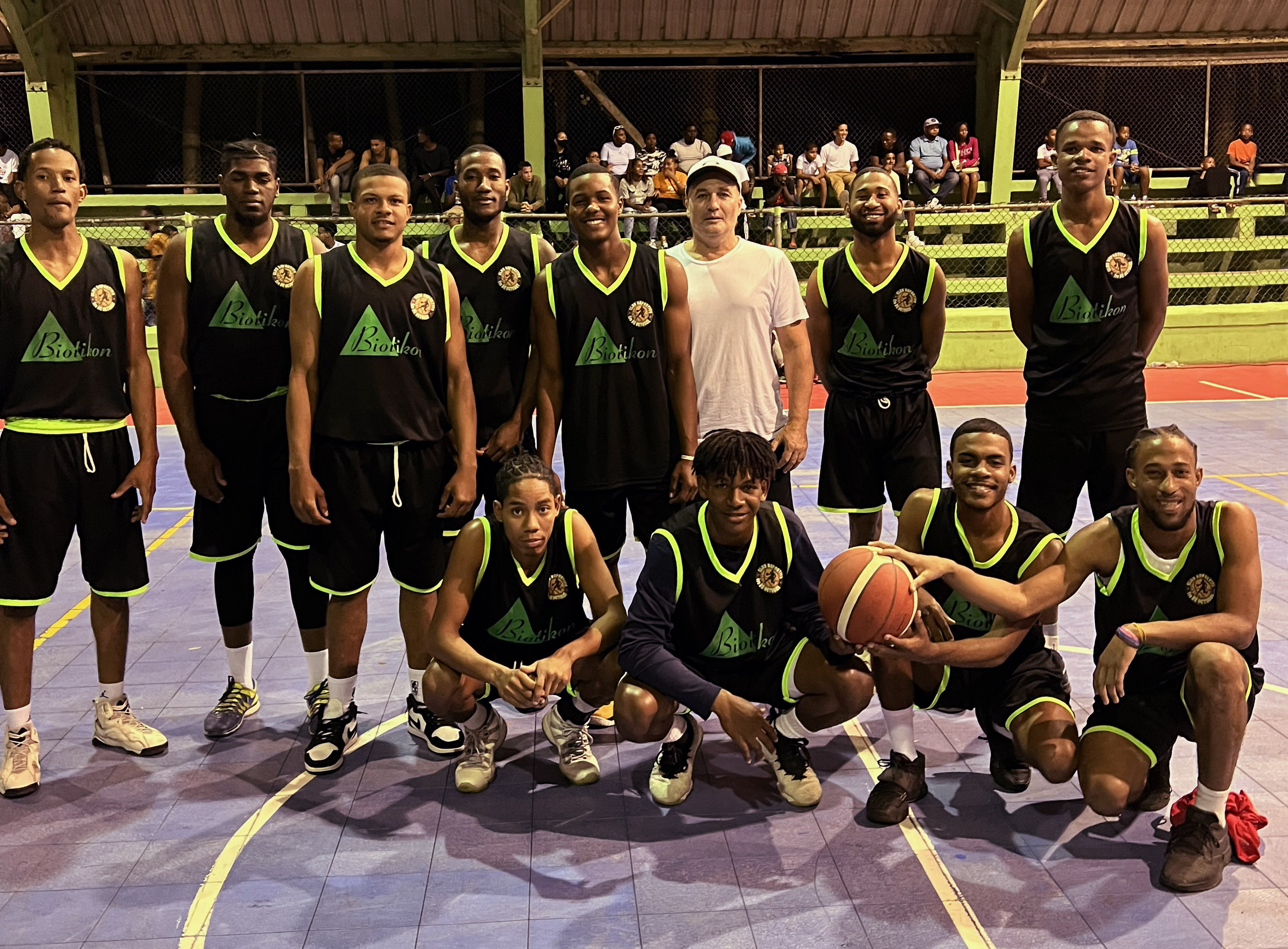 Équipe de Basketball – Photo de Groupe Un groupe de joueurs de basketball en maillots noirs avec accents verts, debout sur le terrain, tenant un ballon et en train de célébrer.